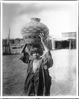Apache girl balances water basket on head